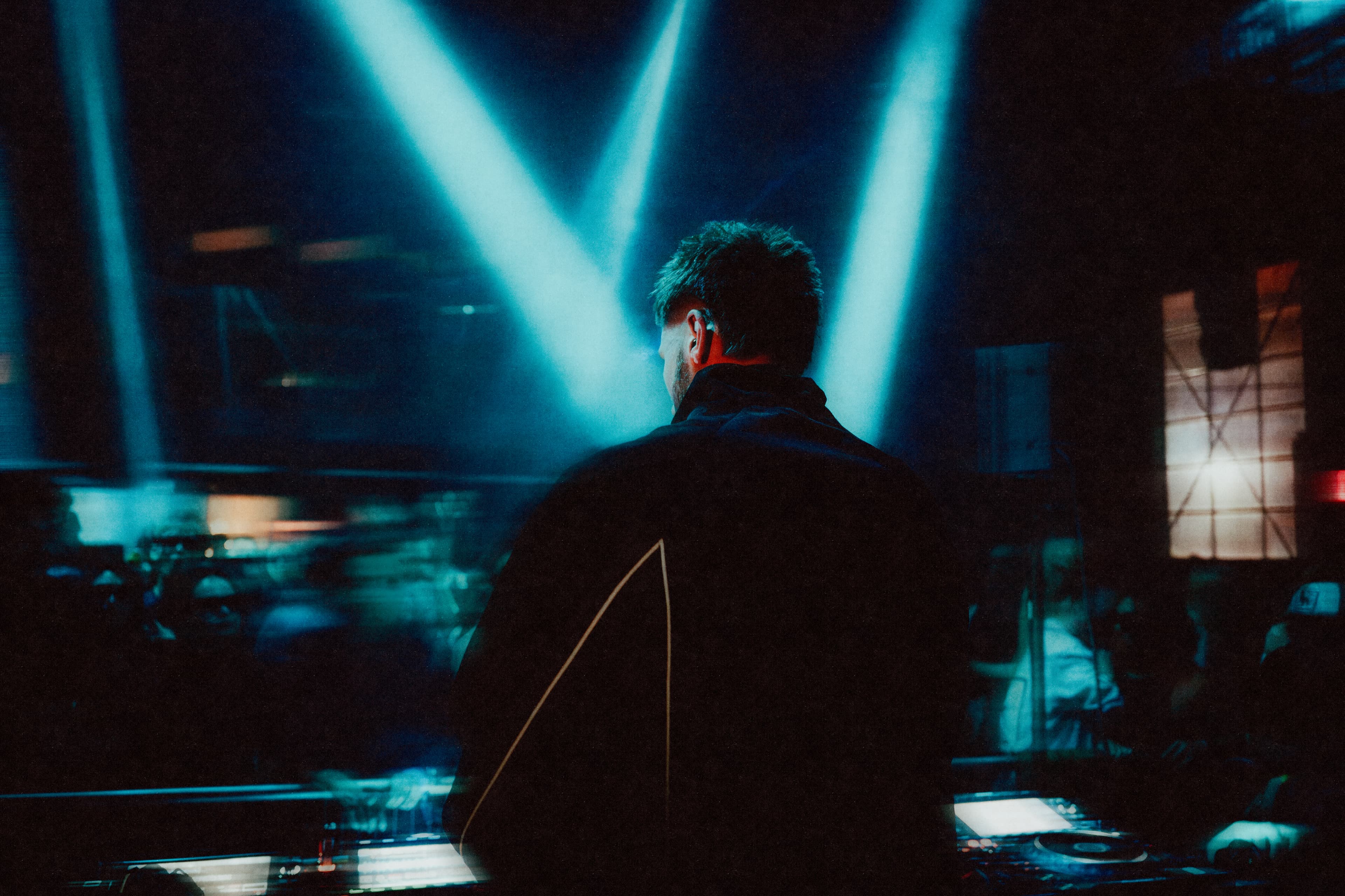 DJ performing at turntables with dynamic neon lighting and energetic dancing crowd visible behind